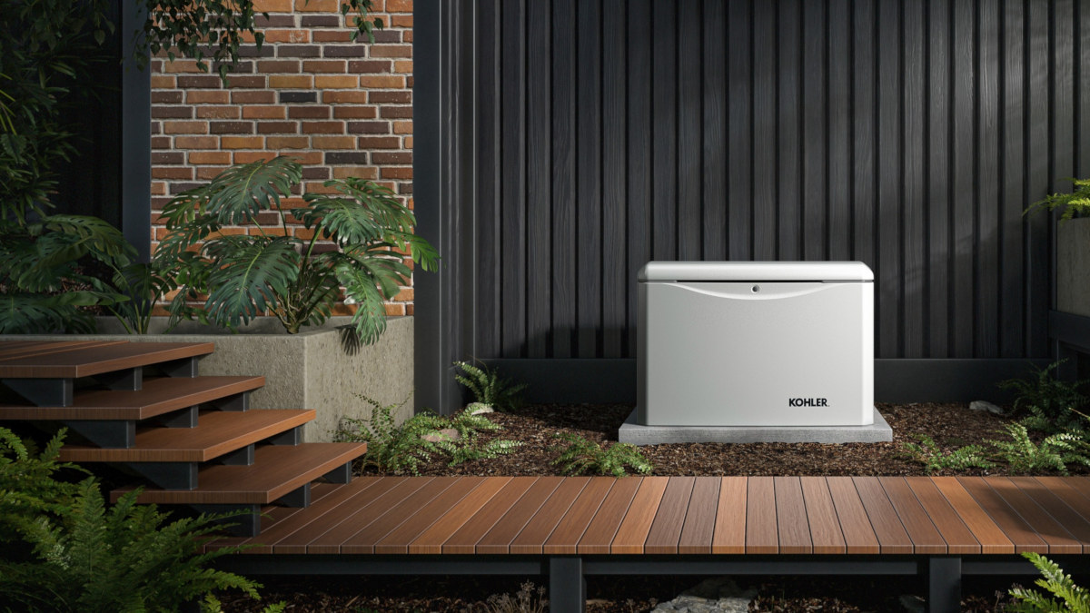 A Kohler home standby generator installed against a house behind a wooden walkway surrounded by landscaping.